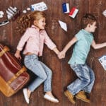 Wycieczki zorganizowane dla szkół i firm – dlaczego dobra organizacja ma znaczenie? To travel is to live. Children lying near travel items. Girl with suitcase