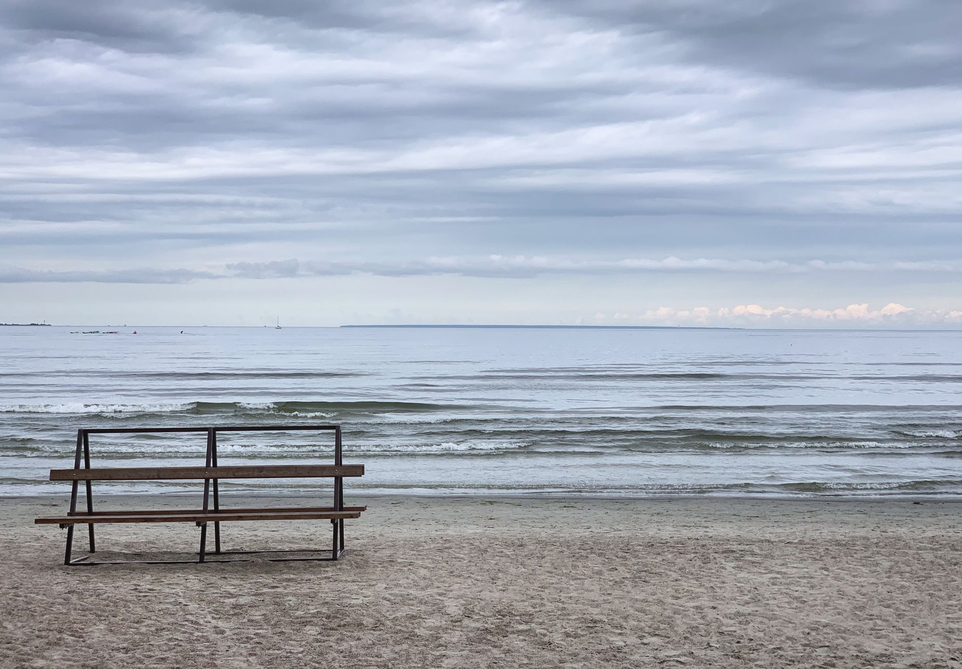 Pusta ławka z widokiem na spokojne Morze Bałtyckie pod pochmurnym niebem