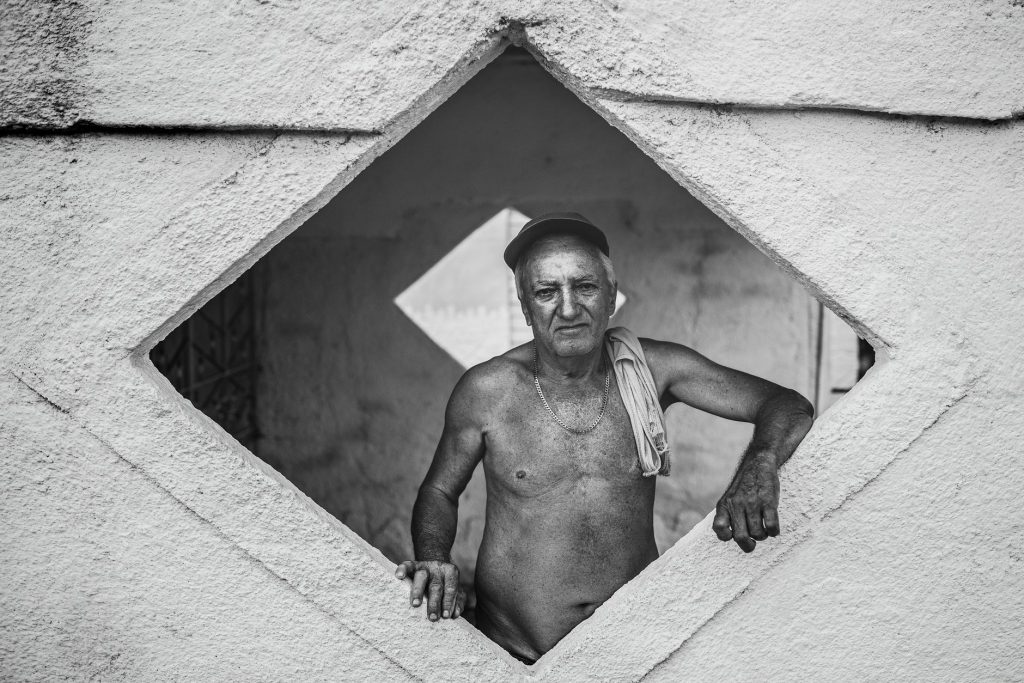 Czarno-biały portret starszego Kubańczyka w geometrycznym otworze muru